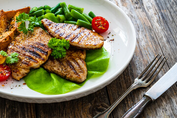 Grilled pork loin steaks with green beans and fried potatoes on wooden table
