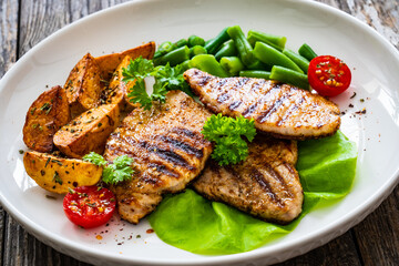 Grilled pork loin steaks with green beans and fried potatoes on wooden table
