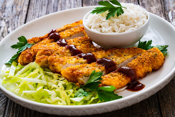 Tonkatsu - crispy Japanese pork chop with white rice and  fresh vegetables on wooden table