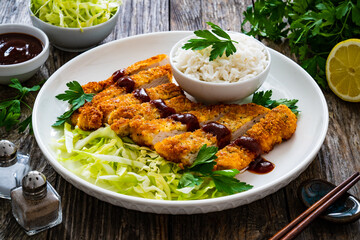 Tonkatsu - crispy Japanese pork chop with white rice and  fresh vegetables on wooden table