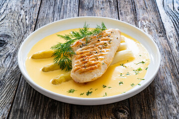 Grilled chicken breast and white asparagus in hollandaise sauce on wooden table
