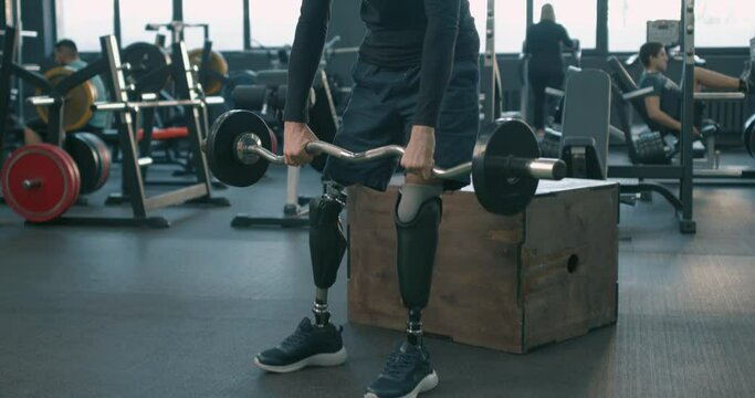athletic motivated strong sportsman with artificial legs working out with barbell at gym, close up photo. Slow motion, concentration, inclusion and diversity. cross fit