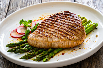 Grilled beef steak with green asparagus on wooden table

