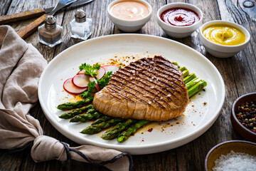 Grilled beef steak with green asparagus on wooden table

