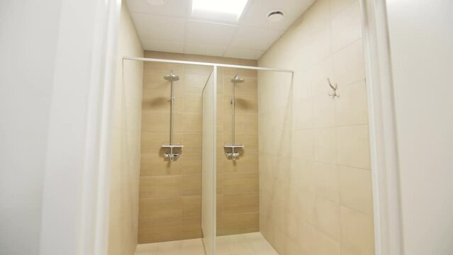 Motion from cloakroom to public shower with separated cabins. Enclosures for clothes storage and body wash in modern sports club