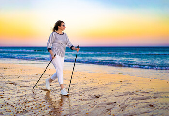 Nordic walking - woman training on beach at sunset

