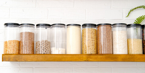 organization of food storage in the kitchen, transparent reusable cans for cereals and pasta on a wooden shelf, a pantry with zero waste