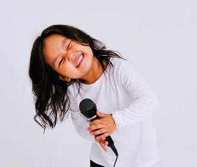 Stylish Asian girl 3 years old, singing songs with a microphone, holding a microphone and dancing in karaoke, posing on a white background. for advertising with copy space