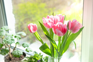 a bouquet of pink tulips in a transparent vase on the windowsill against the background of the window. Bouquet of flowers as a gift to your beloved