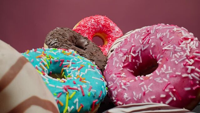 Various colorful donuts. Pile of different delicious donuts. Bakery and food concept. Dolly slider shot with laowa probe lens. Camera moving out from long shot to close. Macro in 4K, UHD