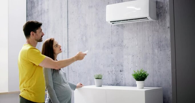 Happy Young Couple Adjusting Temperature Of Air Conditioner