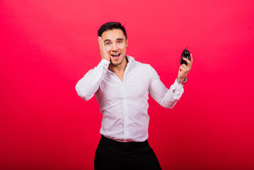 Emotional young man holding clock on red background. Being late concept