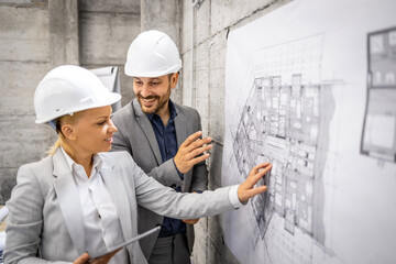 Structural engineers with project plan and tablet computer controlling and inspecting building process.