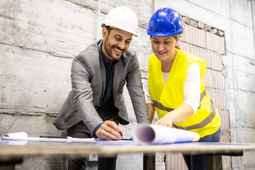 Team of experienced architects and civil engineers analyzing and looking at building plant at construction site.