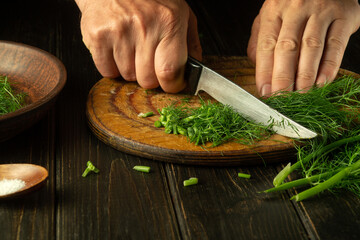 A man hands cut fresh fennel with a knife on a kitchen cutting board before preparing national or vegetarian dishes. Cutting foeniculum at home