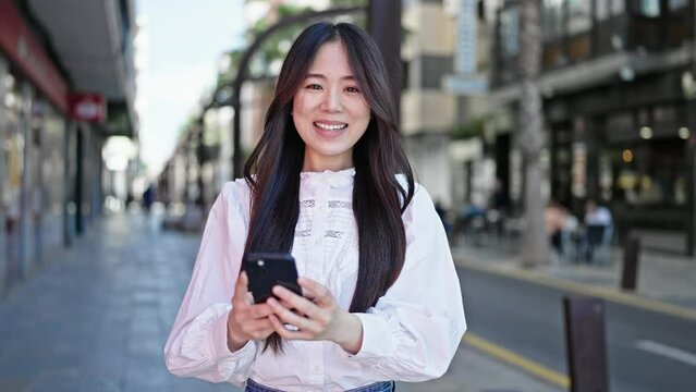 Young chinese woman using smartphone smiling at street