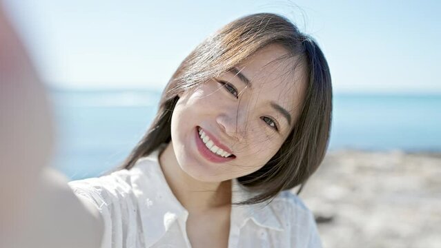 Young chinese woman making selfie by the camera blowing kiss at seaside