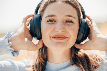 Face of pretty young woman listening to music with wireless headphones outside in nature. Woman with wireless headset on her ears. High quality photo