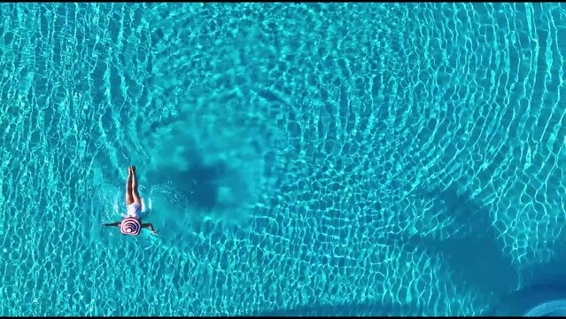 Aerial view with woman in bikini sunbathing as laying on swim ring in swimming pool water in background