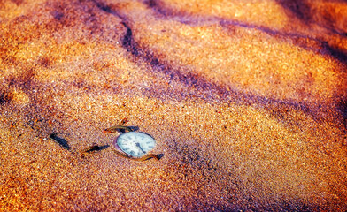 Antique rotten pocket watch buried partial in the sand.