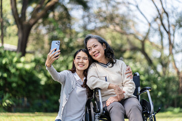 Obraz premium Asian senior woman in wheelchair with happy daughter taking selfie photo with smartphone