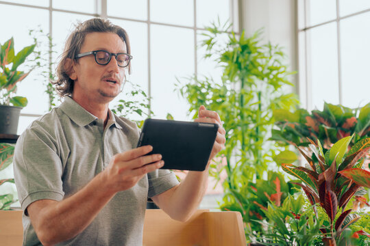 Man in eyeglasses with digital tablet selling garden tree online at glass house, Retirement lifestyle hobby concept