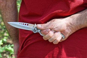 a man in red clothes holds a gray knife behind his back