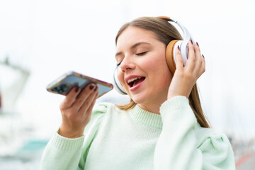 Young pretty blonde woman listening music with a mobile and singing