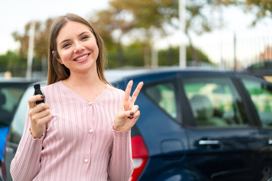 Young pretty blonde woman holding car keys at outdoors smiling and showing victory sign