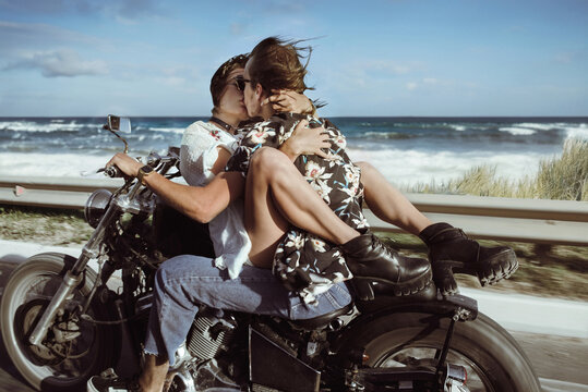 Two lovers hug each other seeting on the oldschool motorcycle and have a kiss at the hight speed near the ocean drive