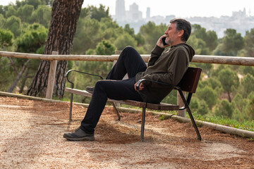 White man on a park bench wearing casual clothes and talking on the phone cheerfully.