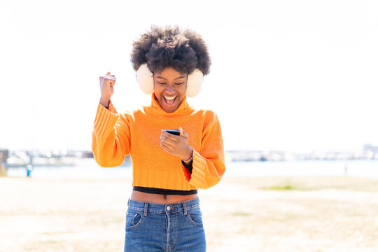 African American girl wearing winter muffs at outdoors surprised and sending a message