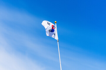 The flag of Korea on the flagpole flutters in the wind against the blue sky