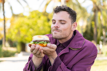 Young caucasian man at outdoors holding a burger