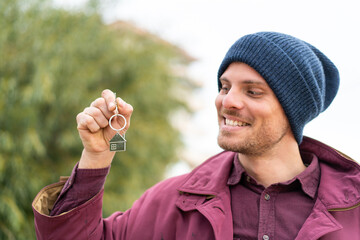 Fototapeta premium Young caucasian man holding home keys at outdoors