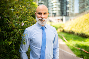 Mature bald stylish business man portrait with a white beard outdoor in a green city
