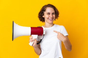 Young English woman isolated on yellow background holding a megaphone and pointing side