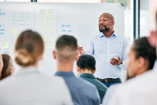 Male speaker, conference and corporate team at training for company with learning on a board with audience. Business, presentation and coach is speaking to employees during a meeting at the office.
