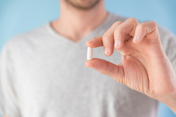Man hold white capsule with collagen in male hand on blue background. Nutritional supplement,...