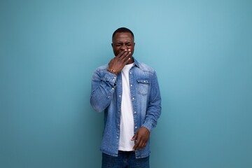 portrait of a young attractive african man dressed in stylish denim clothes covering his face with his hand