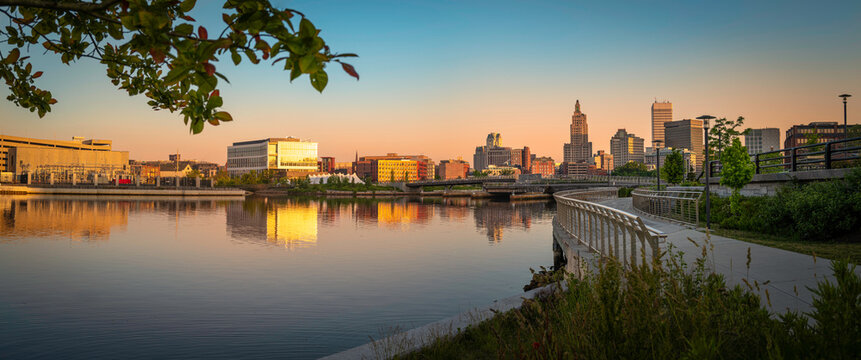 Providence City Riverwalk Skyline at sunrise with warm sunrays reflected on the water and industrial buildings over the riverbank in Rhode Island, tranquil cityscape along the footpath 