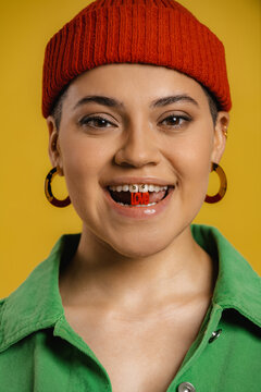 Portrait of beautiful young woman in hat holding plastic letters in mouth against yellow background