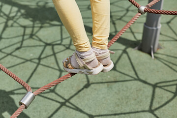 Legs of unrecognizable kid playing on playground walking on rope.