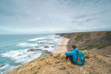 Young man sits above the famous Praia da Carreagem beach in southwest Portugal, near the town of...