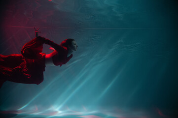 Fototapeta na wymiar a girl under water, in an aquarium, in a pool in a red long dress swims like a mermaid