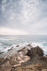 Rocky cliffs with futuristic patterns on the Atlantic coast near the town of Aljezur in southwestern Portugal. The sound of the ocean as the sun sets. Wandering the Rota Vicentina