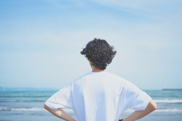 夏の海岸に向かって立つTシャツ姿の男性