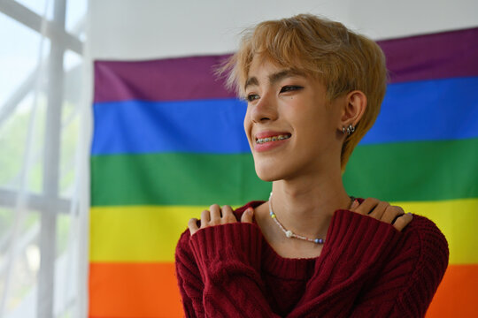 Portrait with Young LGBT teenage boy hugging himself and happily smiling, pride flag on the background, Hug of self love, Butterfly Hug.