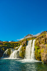 Wonderful waterfall named Kirkjufellsfoss with a Kirkjufell church like iconic mount in Western Iceland, at blue sky and sunny day