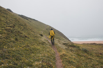 Wandering in heavy rain and wearing a raincoat along the Fisherman Trail in the southern part of Portugal during rainy weather heading to Cape St. Vicente. Rough landscape